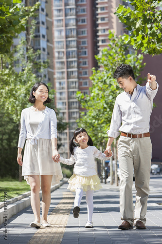 Young parents with daughter strolling on sidewalk hand in hand