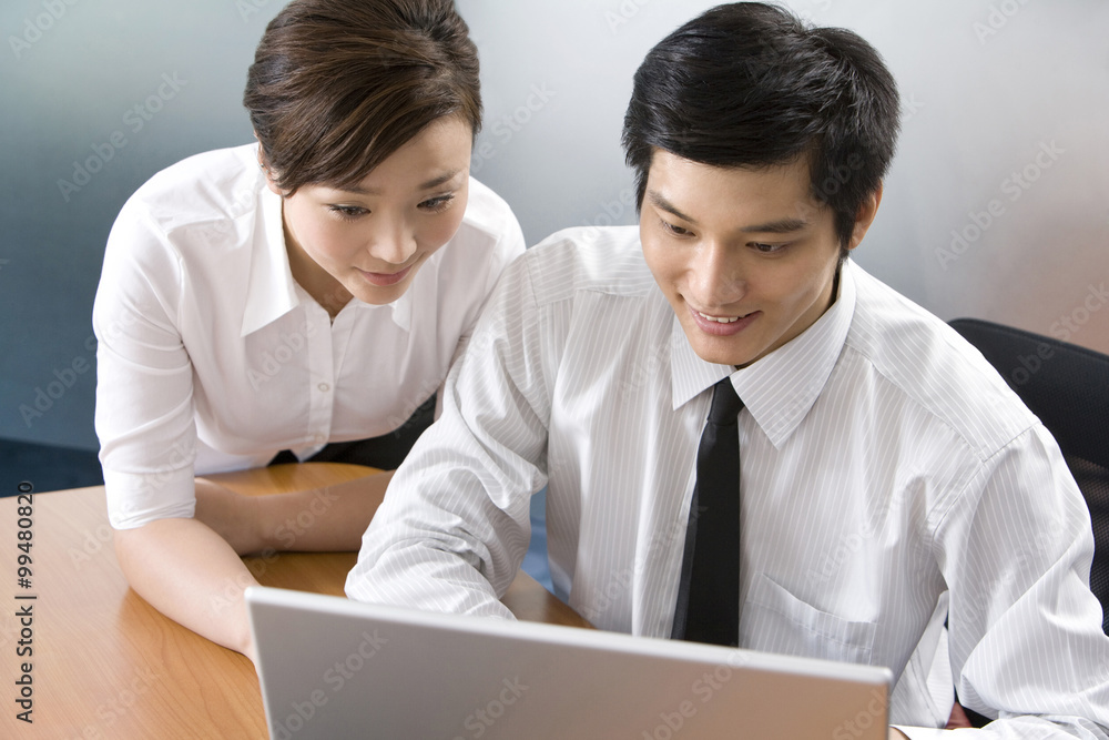 Young businessman and businesswoman using laptop in office Young businessman and businesswoman using laptop in office
