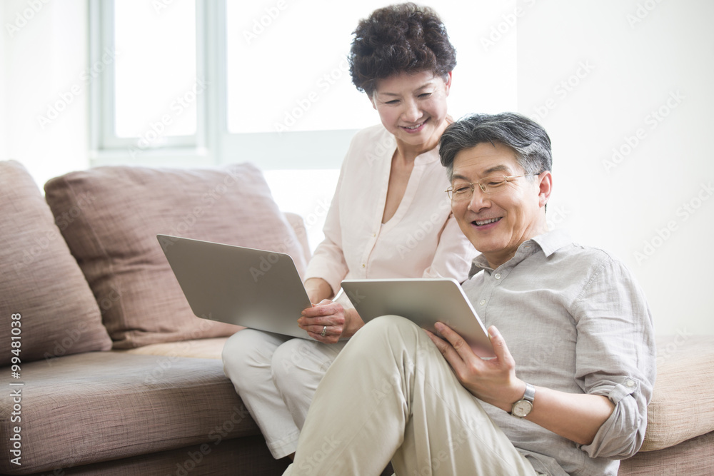 Happy senior couple with laptop and digital tablet