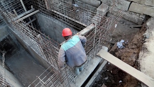 Worker at construction site. Unfinished construction. Building of foundation. Builder with red hard hat at project site photo