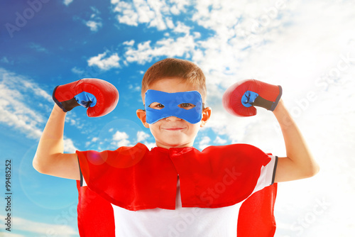 Boy dressed as superhero with boxing gloves on sky background photo