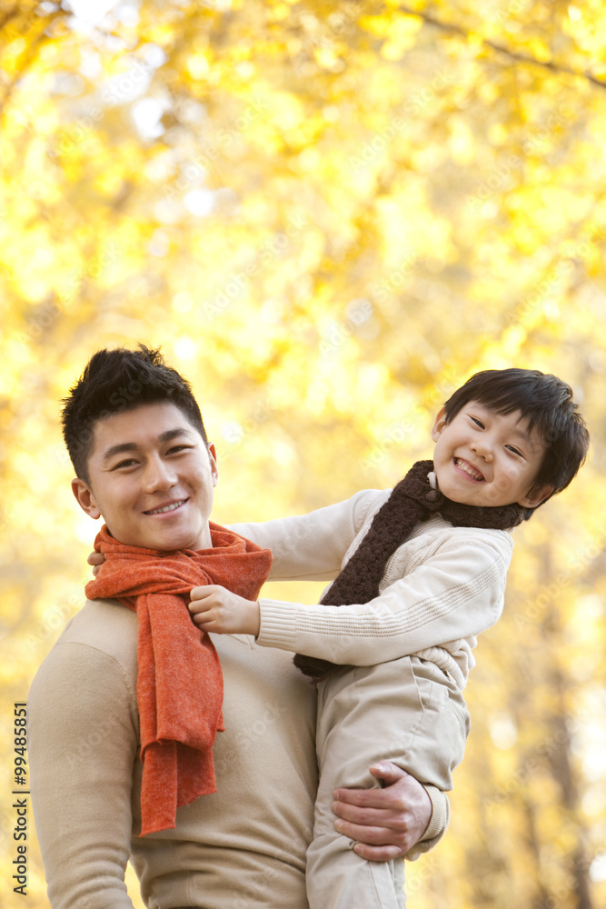 Father carrying son surrounded by Autumn trees in the background Father carrying son surrounded by Autumn trees in the background