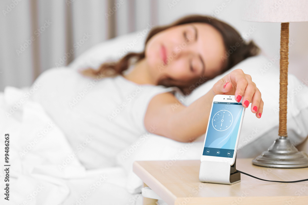 Beautiful young woman waking up with mobile alarm clock Beautiful young woman waking up with mobile alarm clock