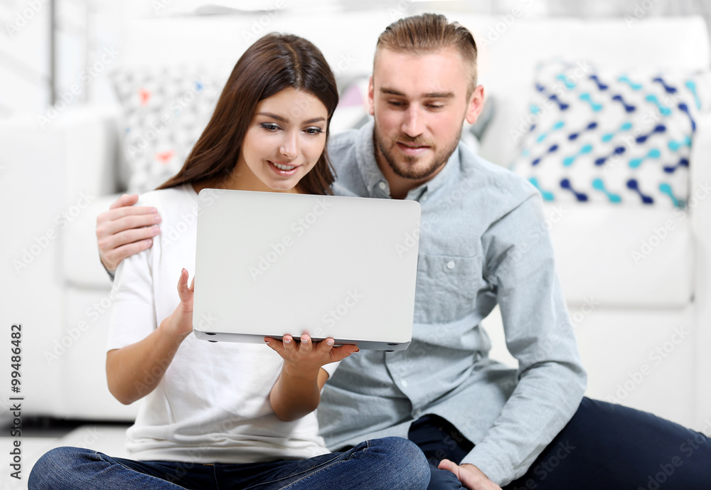 Happy couple sitting on the floor and working on laptop in a room Happy couple sitting on the floor and working on laptop in a room