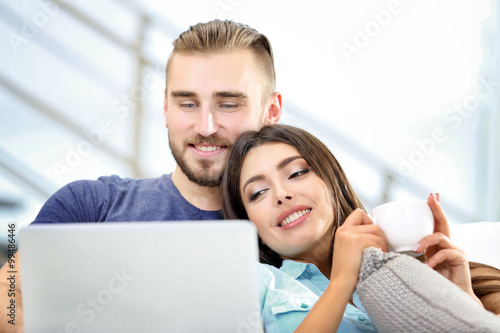Happy couple sitting on sofa with coffee and working on a laptop