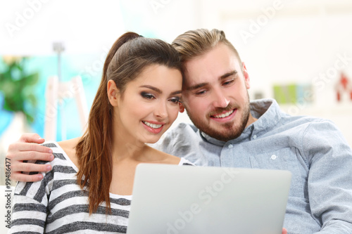 Happy couple sitting on sofa and working on a laptop