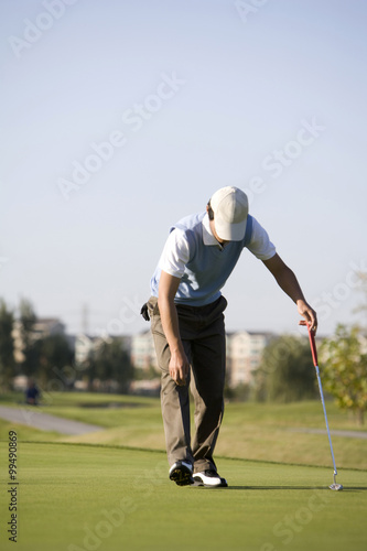 Man picking up golf ball from golf hole