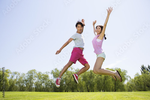 Cheerful young man and young woman jumping on grass