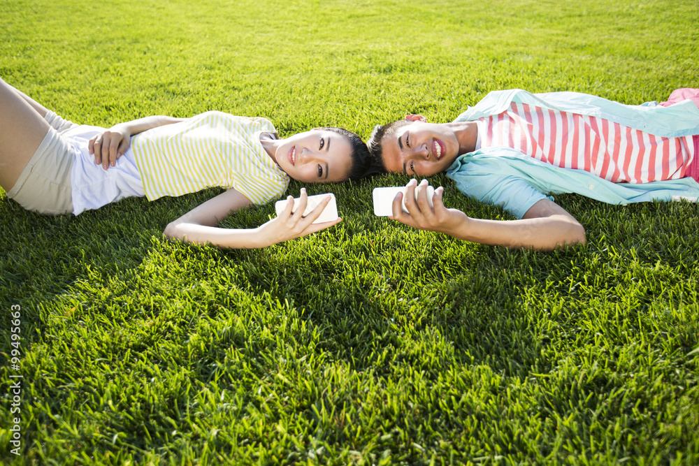 Cheerful young couple lying on grass with cell phones