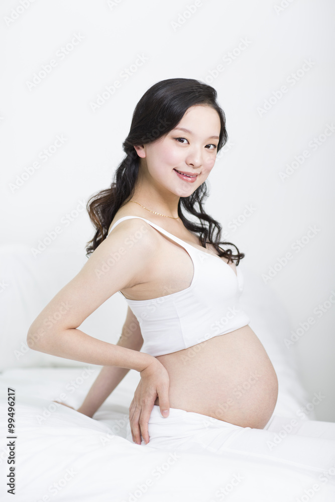 Happy pregnant woman sitting on bed Happy pregnant woman sitting on bed