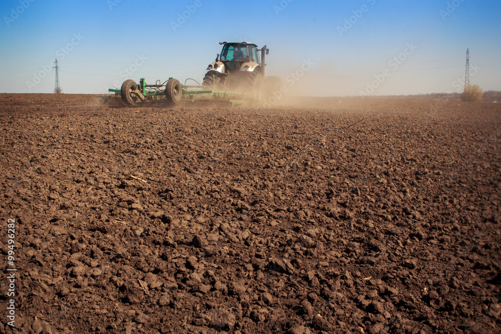 Fototapeta premium tractor cultivator raises great dust on soil
