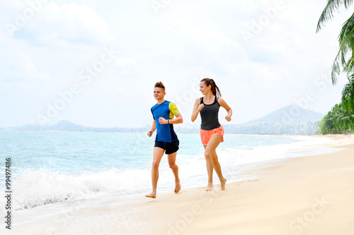 Exercising. Happy Smiling Sporty Runner Couple Running On Beach. Athletic Woman And Fit Man Jogging Near Sea ( Ocean ) During Outdoor Workout. Sports, Fitness. Healthy Lifestyle. Health Concept