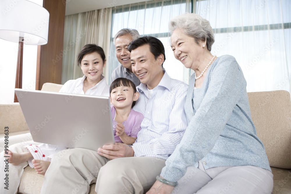 Fototapeta premium Grandparents and Parents with daughter look at Laptop on a sofa