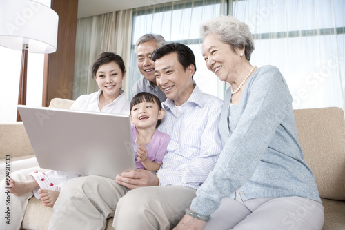 Grandparents and Parents with daughter look at Laptop on a sofa