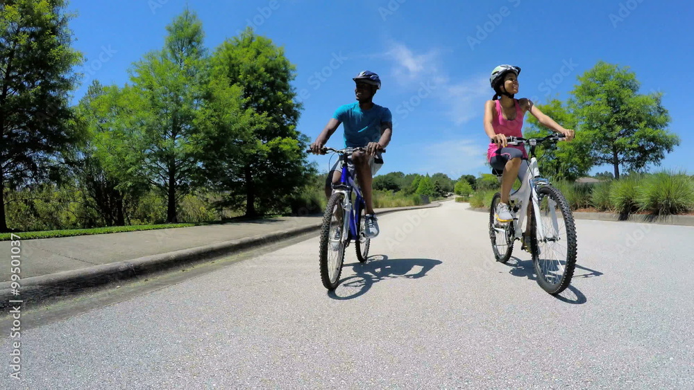 Young active African American man and woman cycling to keep fit outdoors Young active African American man and woman cycling to keep fit outdoors