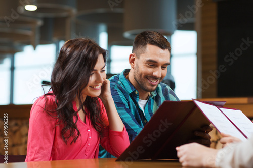 smiling couple with menus at restaurant