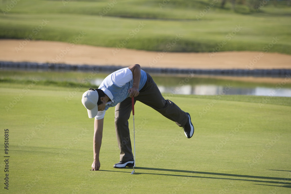 Obraz premium Man picking up golf ball from golf hole