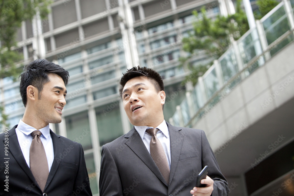 Happy coworkers walking and chatting with smart phone in hand outdoors, Hong Kong Happy coworkers walking and chatting with smart phone in hand outdoors, Hong Kong