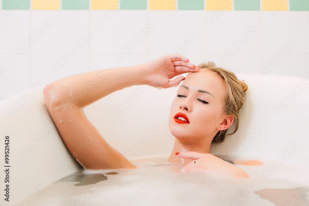 Obraz premium Passionate young caucasian blonde girl with long hair beautiful legs and bright red lipstick lying in white bathroom
