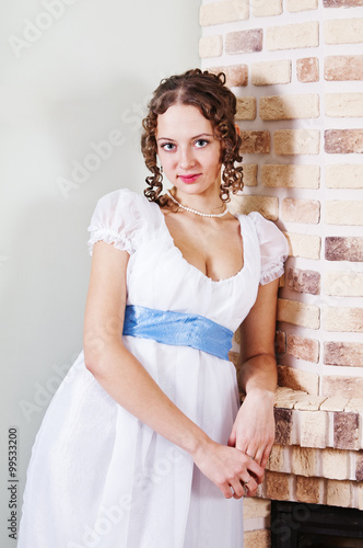 Girl in ancient dress standing near fireplace