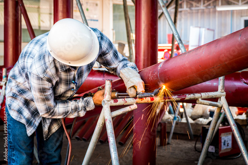 Worker cutting steel red pipe with acetylene welding cutting torch. Industrial construction site background. photo