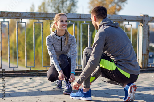 smiling couple tying shoelaces outdoors