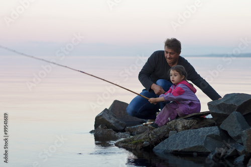 Father and daughter fishing on lake at sunset