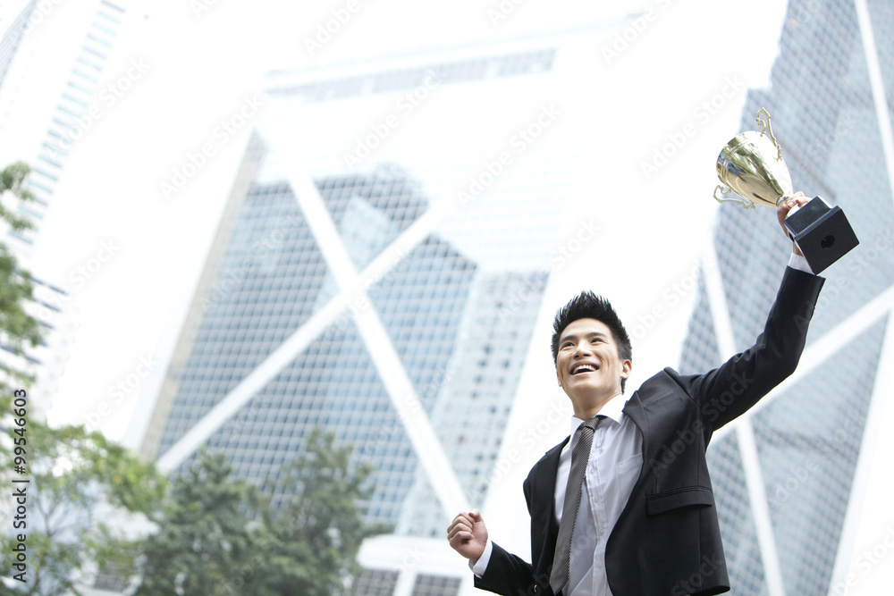 Excited young businessman jumping with a trophy in hand, Hong Kong Excited young businessman jumping with a trophy in hand, Hong Kong