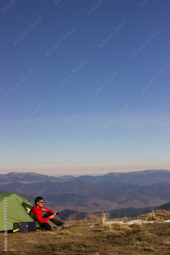 The solar panel attached to the tent. The man sitting next to mobile phone charges from the sun. The solar panel attached to the tent. The man sitting next to mobile phone charges from the sun.