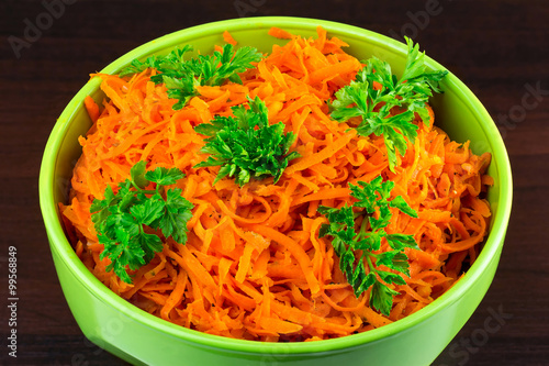Spicy salad of grated carrots in bowl on wooden background