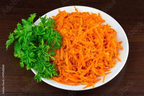 Spicy salad of grated carrots in bowl on wooden background