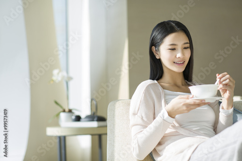 Happy young woman eating porridge on sofa