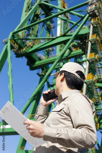 Male shipping industry worker talking on walkie-talkie with crane in the background