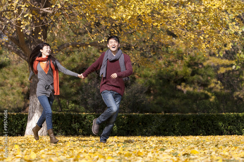 Cheerful young couple in love running on the lawn in autumn