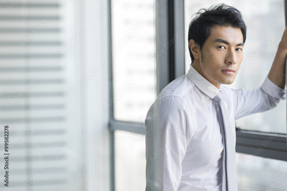 Young businessman standing by window Young businessman standing by window