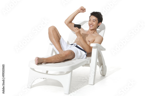 Young man using mobile phone on sand chair