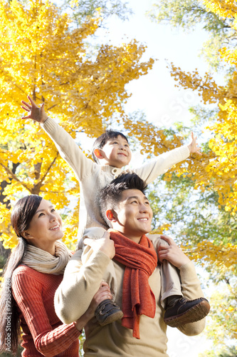 Boy sitting on his father's shoulders in a park with family in Autumn