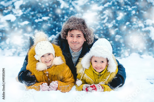 The father with little daughters in the winter wood smile lying on snow