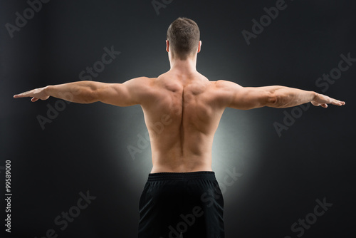 Rear View Of Muscular Man Standing Arms Outstretched