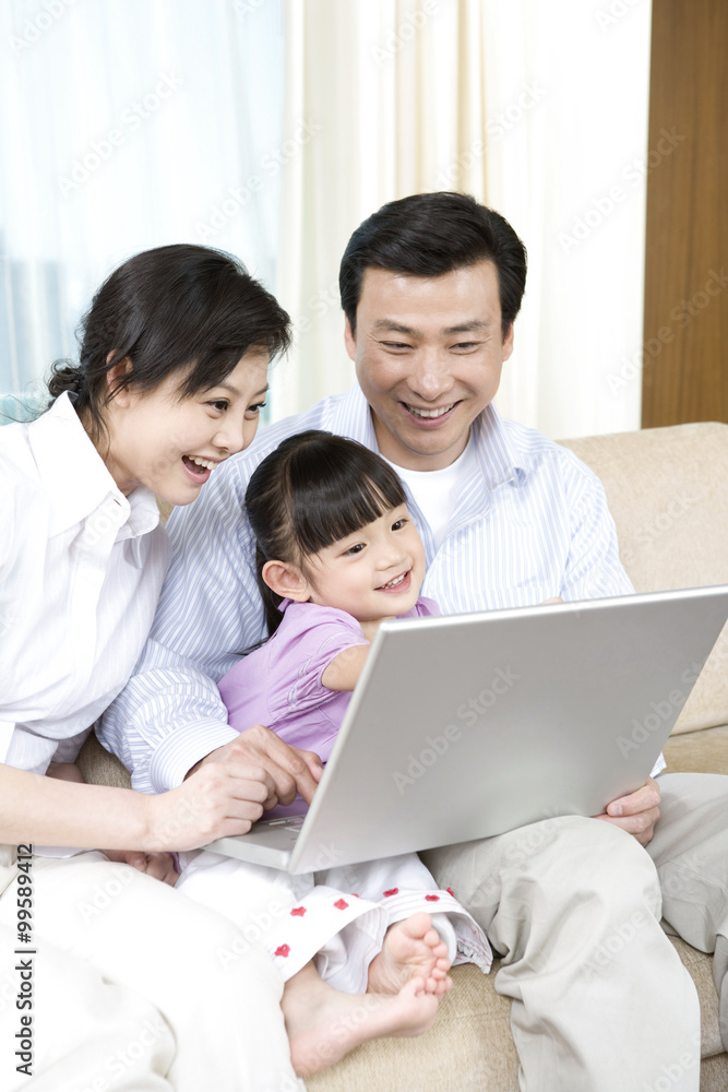 Young couple and daughter look at laptop on sofa