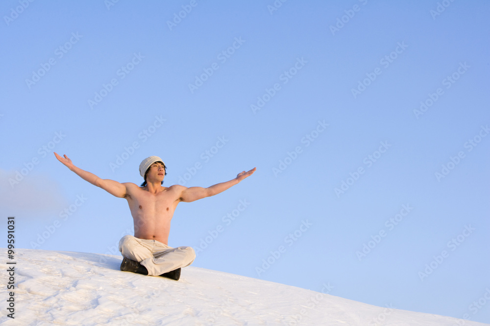 Young man raising his arms while sitting in snow Young man raising his arms while sitting in snow