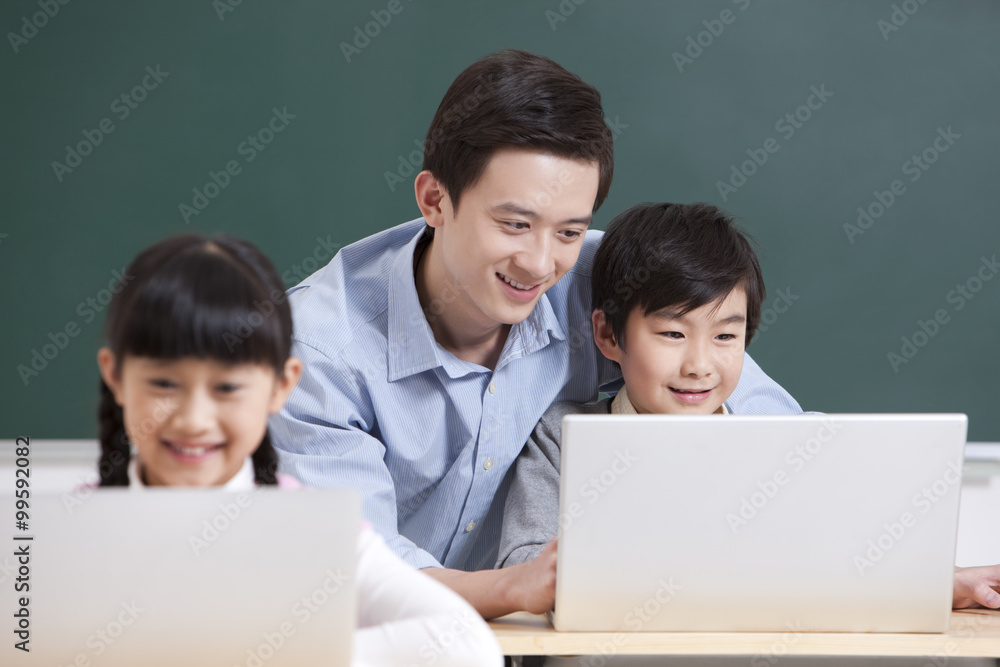 Happy schoolchildren using laptop under teacher's guidance Happy schoolchildren using laptop under teacher's guidance