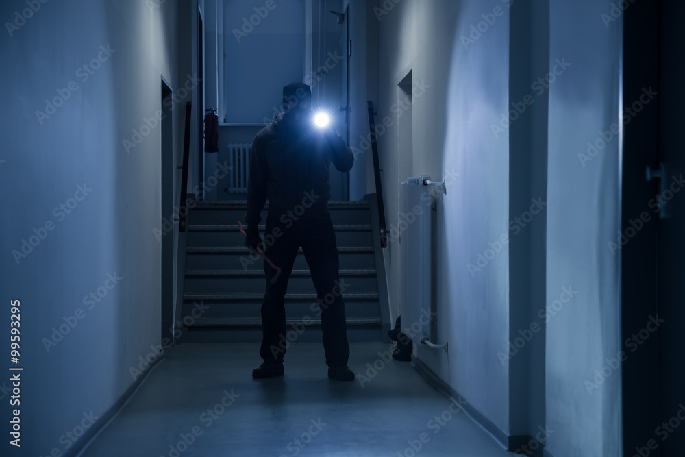 Burglar With Flashlight And Crowbar In Office Corridor