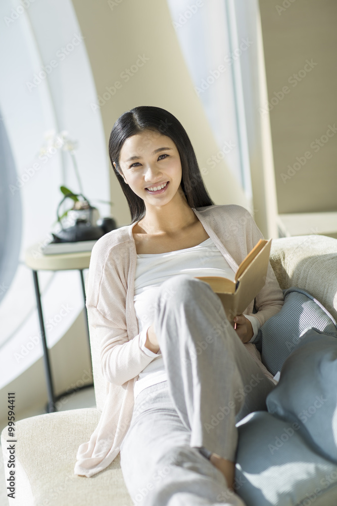 Happy young woman sitting on sofa with a book Happy young woman sitting on sofa with a book