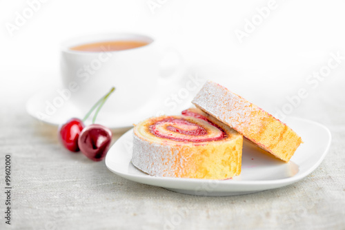 roll with cherries on plate and cap of tea, close up