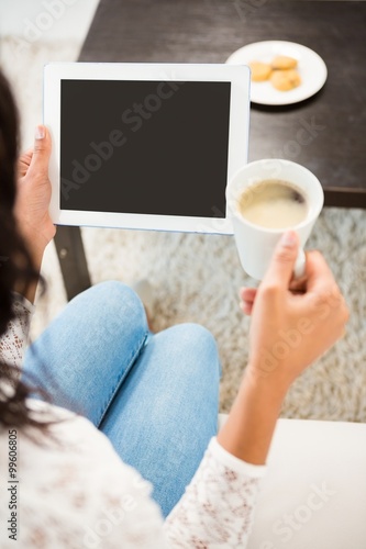 Over shoulder view of woman using tablet while holding coffee