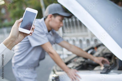 Car owner messaging on mobile phone next to broken down car
