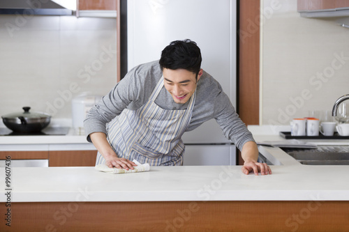 Cheerful young man cleaning kitchen