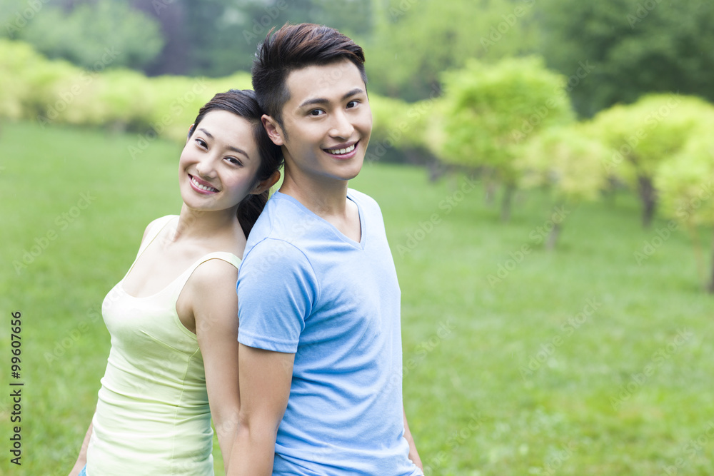 Sweet young couple in park, back to back Sweet young couple in park, back to back