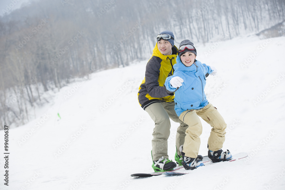 Young man teaching girlfriend to snowboard